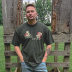 Man wearing a dark green t-shirt with text and graphics, standing in front of wooden pallets.